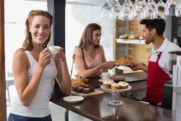 Woman drinking coffee with friend and male barista in coffee sho
