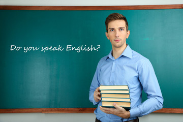 Young teacher with books near chalkboard in school classroom