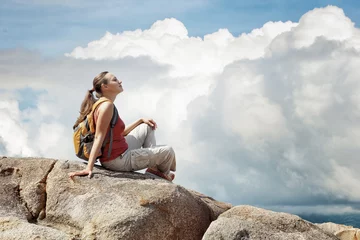 Tuinposter Young woman sitting on a rock with backpack. © soft_light