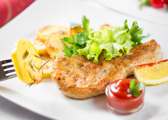 Roasted pork chop with potatoes, ketchup and lemon on dish