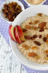 Tasty oatmeal with raisins and apples on wooden table