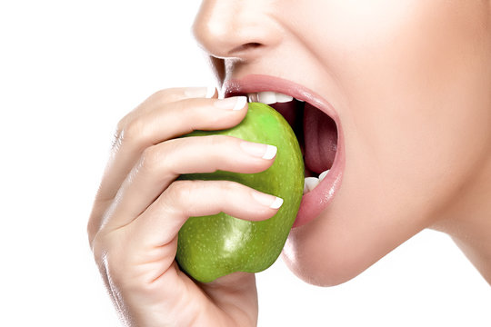 Vegetarian woman with a healthy mouth biting a big green apple in a cropped portrait on white with copyspace