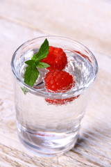 Water in glass with two raspberries and mint