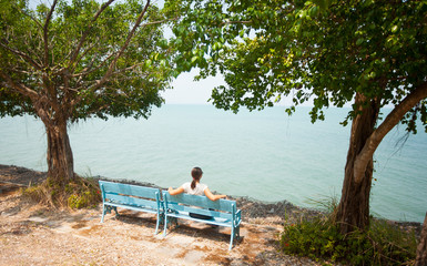 Fototapeta premium Young woman sitting on bench facing the sea