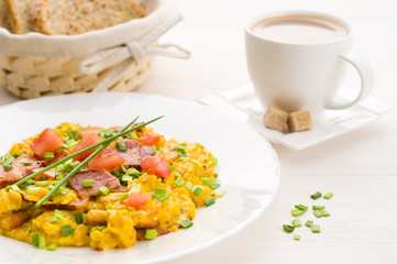 Scrambled eggs and bacon on white table