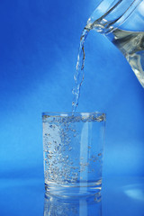 Pour water from  pitcher into  glass, on dark blue background