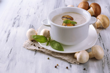 Mushroom soup in white pot, on napkin, on wooden background
