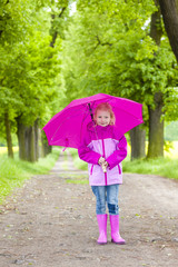 little girl wearing rubber boots with umbrella in spring alley