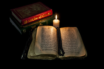 A Quran with open pages, a black rosary inside and a burning candle