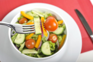 fork with cherry tomato, carrot and cucumber in fresh salad bowl