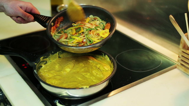 man's hands mixing vegetables and chicken curry in a frying-pan