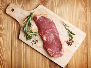 Raw sirloin steak with rosemary and spices on cutting board