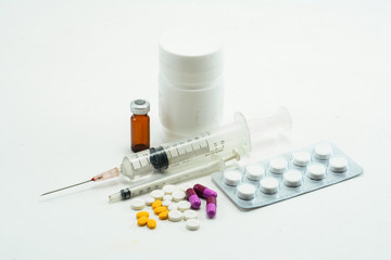 Pills spilling out of pill bottle and Syringe isolated on white 