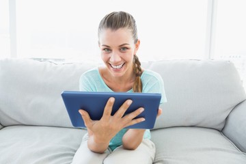 Cheerful woman sitting on couch using tablet pc