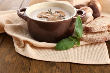 Mushroom soup in pot, on wooden background