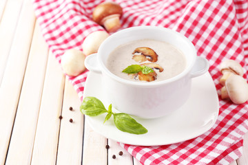 Mushroom soup in white pot, on napkin, on wooden background