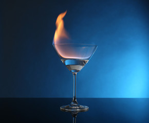 Glass with burning alcohol on blue background