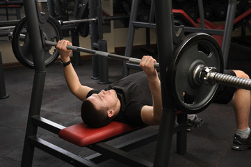 young man doing bench press workout in gym