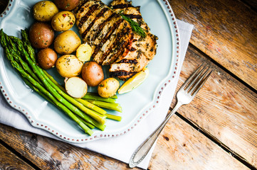 Grilled chicken with potatoes and asparagus on wooden background