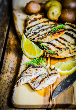 Grilled chicken with potatoes and herbs on wooden background