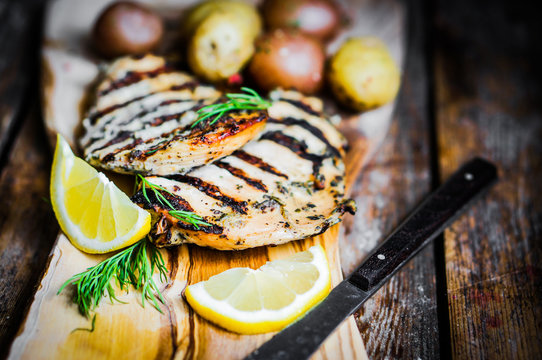 Grilled chicken with potatoes and herbs on wooden background