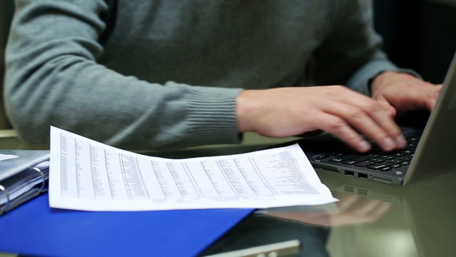 Businessman working on laptop and comparing documents.
