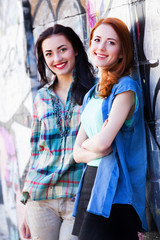 Two girls near graffiti wall.