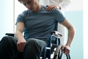 Fototapeta na wymiar Doctor consoling young man sitting in wheelchair