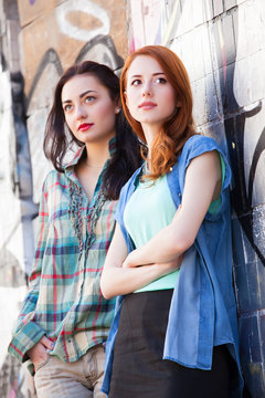 Two girls near graffiti wall.