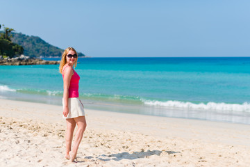 Fototapeta premium Young woman in pink top and beige skirt walking on beach