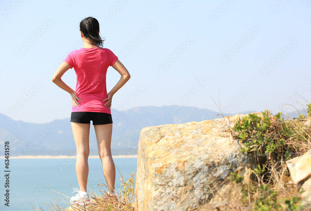 Wall mural woman hiker enjoy the view at seaside mountain rock