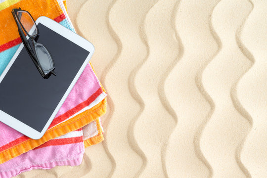 Tablet and glasses on a colorful beach towel