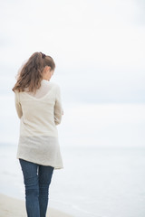 Young woman walking on cold beach. rear view