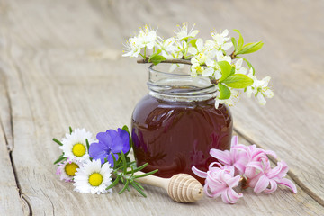 Obraz na płótnie Canvas Honey in a jar, flowers and honey dipper on wooden background