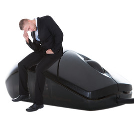 Worried businessman sitting on a computer mouse
