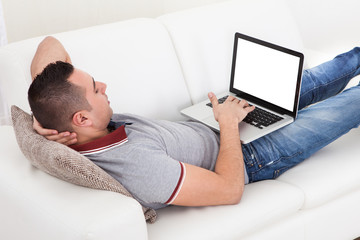 Man Using Laptop While Lying On Sofa