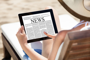 Woman Reading Newspaper On Digital Tablet At Beach