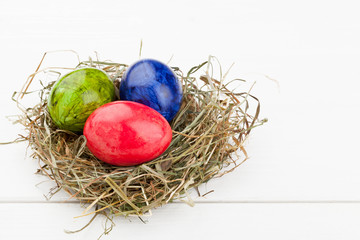 Easter eggs in hay nest on white wood