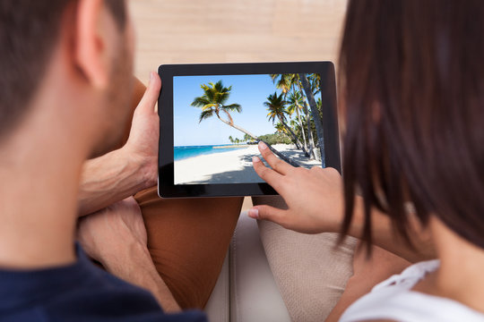 Young Couple Looking Photos On Digital Tablet Together