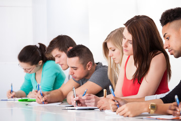 Row Of College Students Writing At Desk
