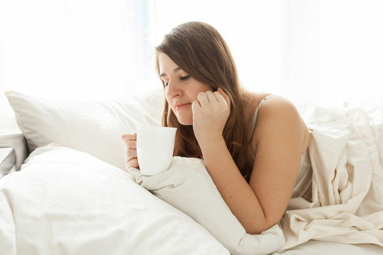 cute woman lying in bed with cup of coffee