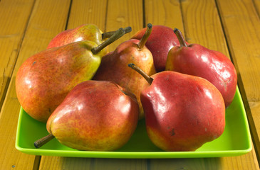 Many red and yellow pears lays in green plate on wooden desk
