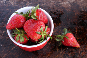 Strawberries in red bowl on brown rustic background