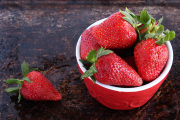 Strawberries in red bowl on brown rustic background