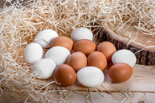 Brown and white eggs in the straw nest on wooden background