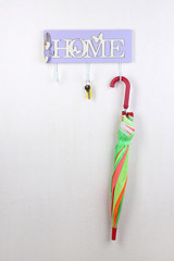 Umbrella and key hanging from hook, on light wall background