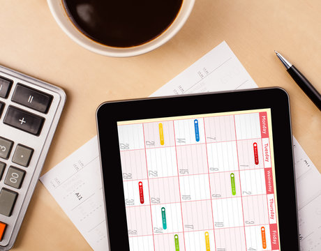 Tablet pc showing calendar on screen with a cup of coffee on a d