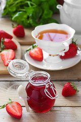 Fresh strawberry jam in glass jar with rooibos tea in white cup