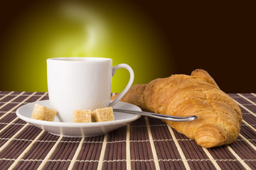 Cup of hot coffee with sugar spoon and croissant