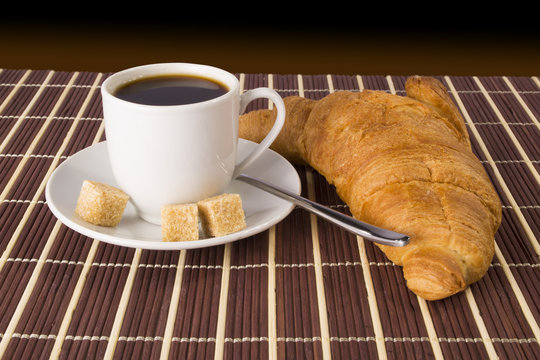 Cup of coffee and a croissant on the mat